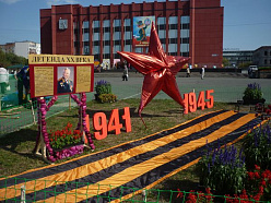 Портрет Михаила Калашникова среди цветочной георгиевской ленты